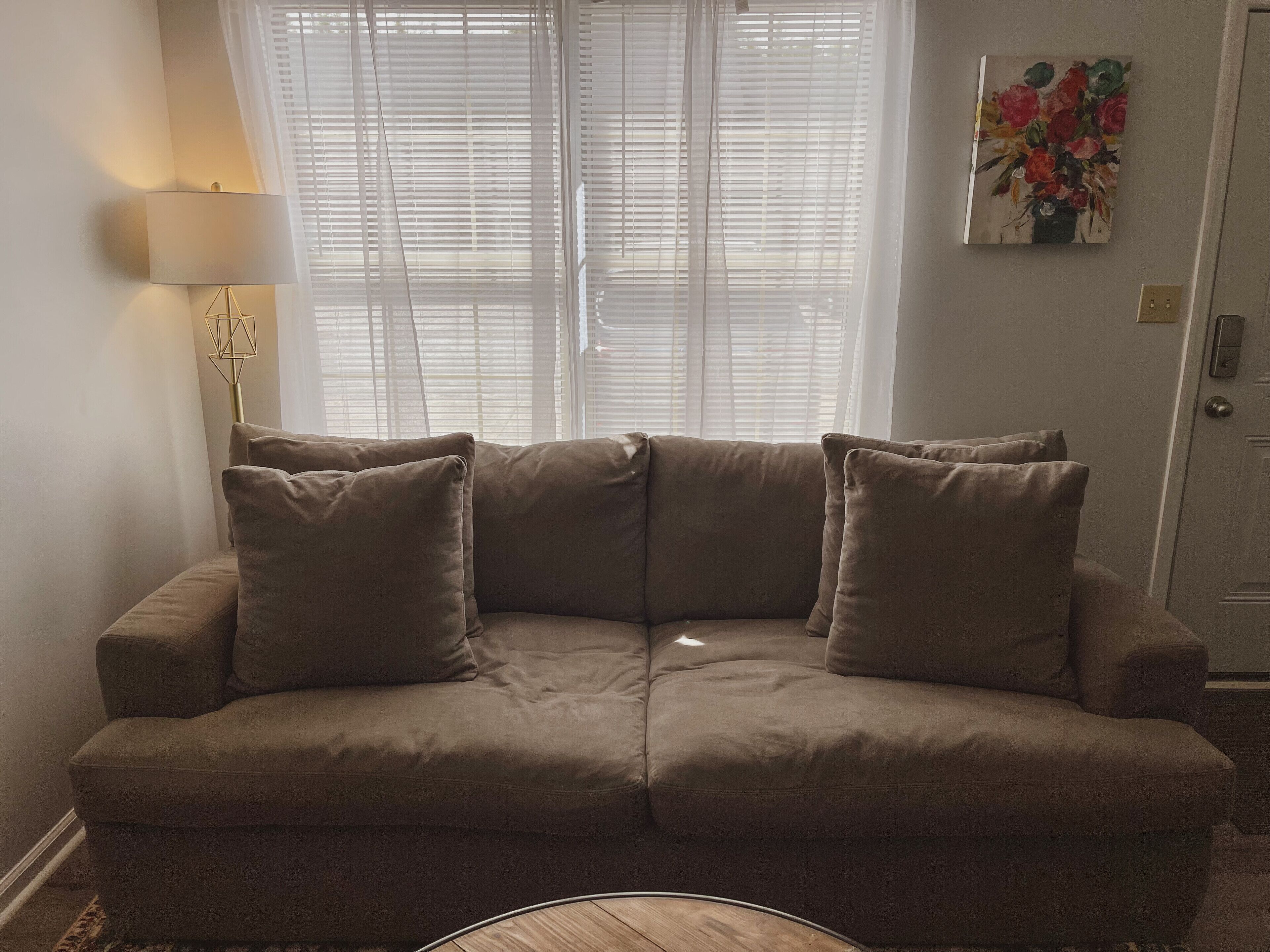 A beige sectional sofa with two cushions, a floor lamp, and a painting of flowers on the wall.