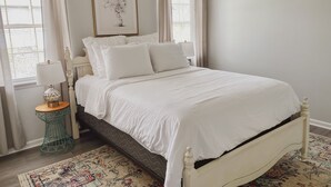 Une chambre à coucher bien rangée, avec un lit, une table de chevet dotée d’une lampe, une œuvre d’art encadrée au mur et un tapis à motifs sur le sol.