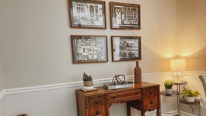 Un bureau en bois avec des tiroirs, un vase et un plateau sur lequel se trouve une plante. Des tableaux encadrés sont accrochés au mur au-dessus du bureau.