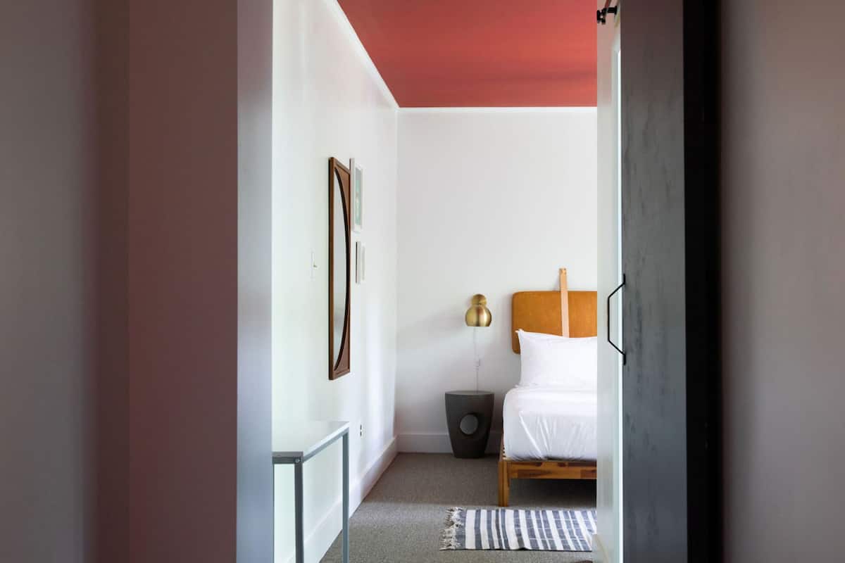 Quarto com cama, mesa de cabeceira, abajur e quadro na parede.