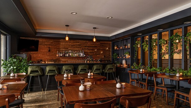 A restaurant with wooden tables and chairs, a bar area with bottles, and green chairs. - THE DARBY (Beach Lake)