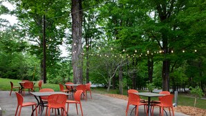 An outdoor patio with tables and chairs, surrounded by trees and string lights. - THE DARBY (Beach Lake)