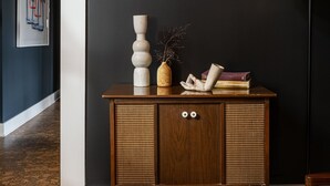 A dark room with a wooden cabinet, a lamp, and a framed picture on the wall. - THE DARBY (Beach Lake)