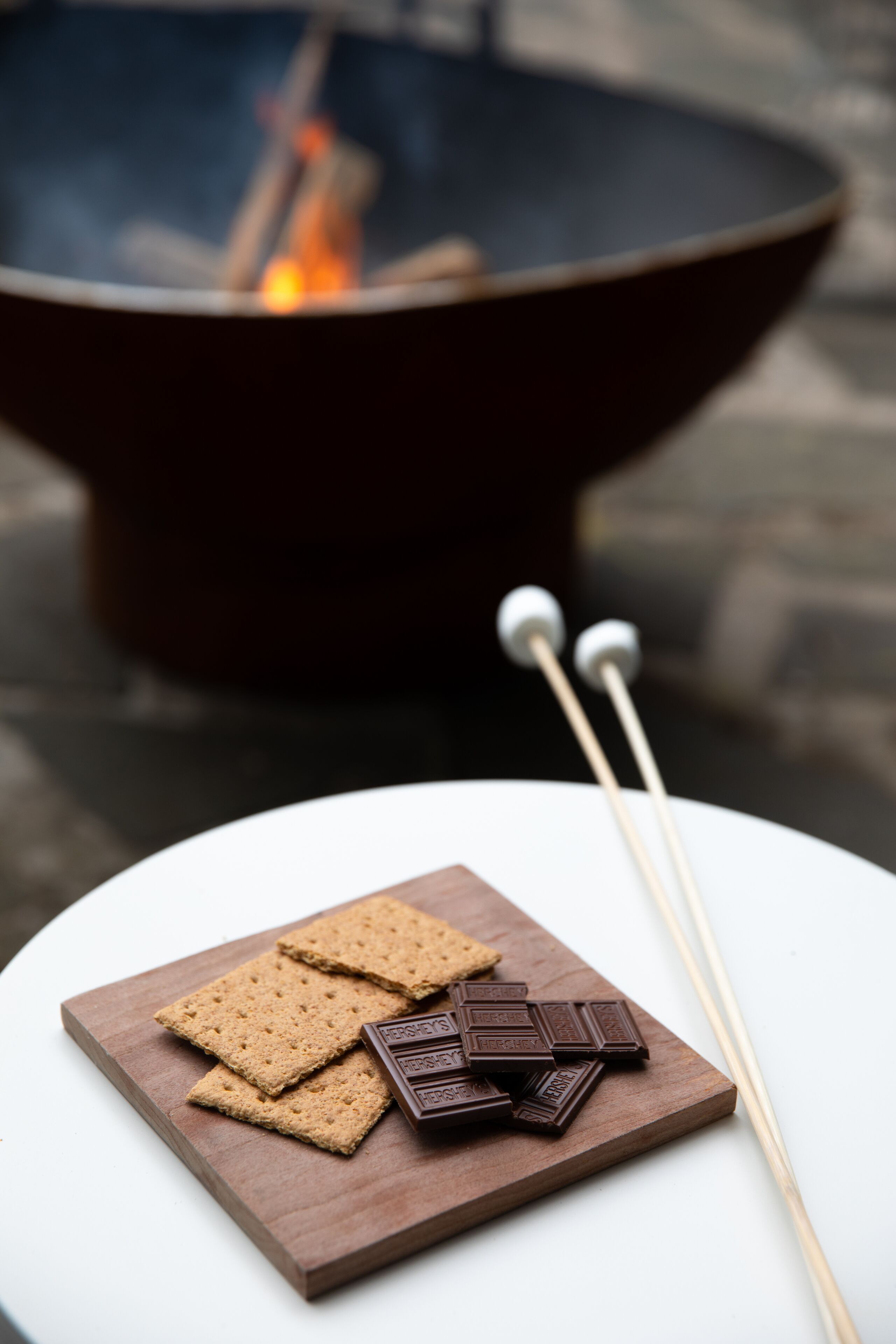 A wooden board with graham crackers and chocolate pieces, with two skewers nearby.