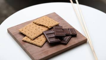A wooden board with graham crackers and chocolate pieces, with two skewers nearby.