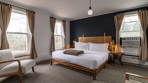 A bedroom with a wooden bed, a bedside table with a lamp, a chair, and a window with curtains. - THE DARBY (Beach Lake)