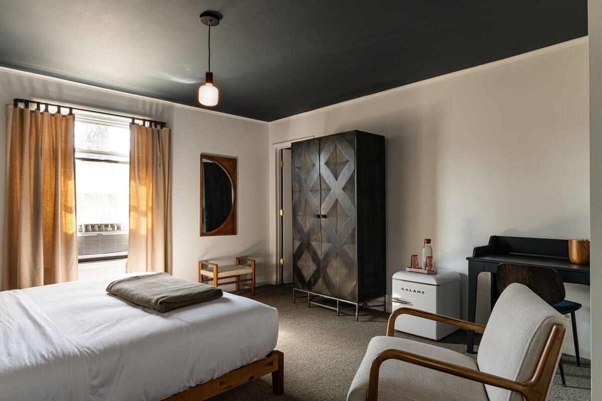 Quarto de hotel com cama, escrivaninha, armário e cadeira.