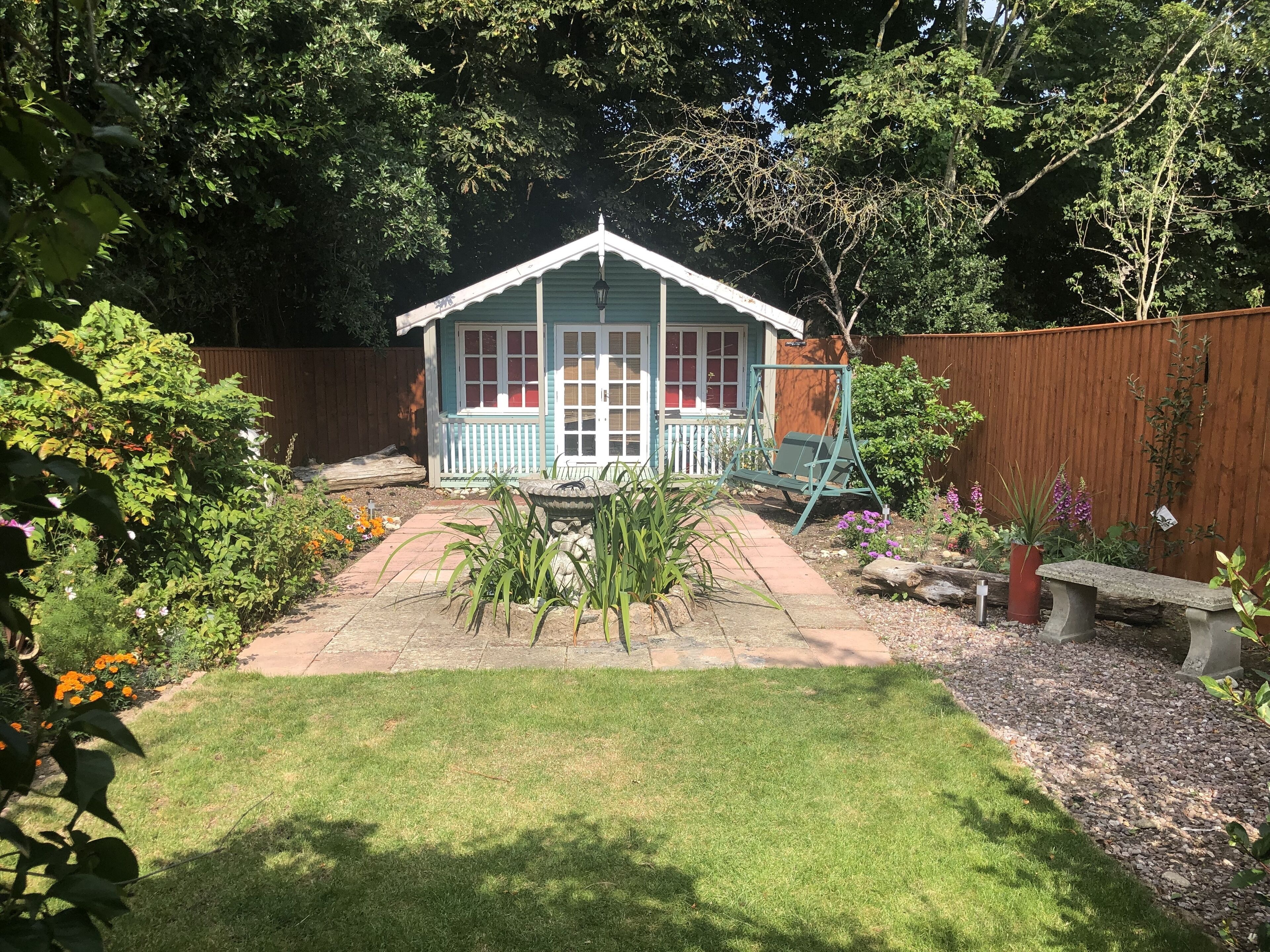 A small, single-story house with a porch, surrounded by a garden with various plants and flowers.