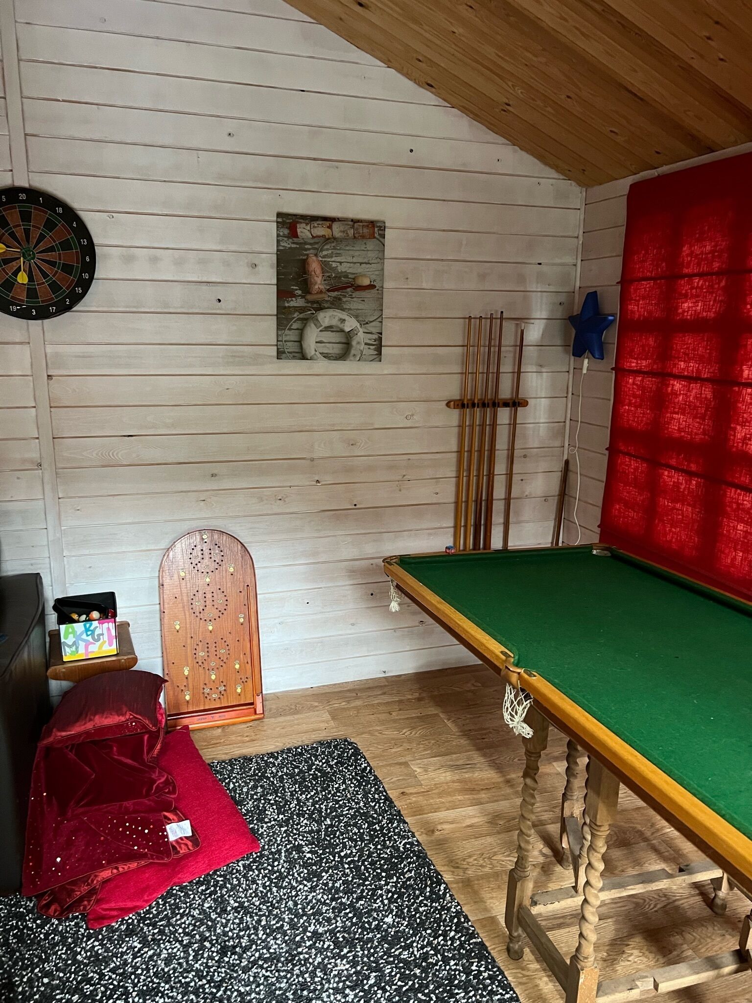 A room with a pool table, a dartboard, a snooker table, and a red curtain.