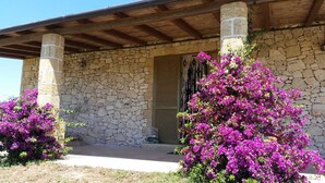 Een stenen gebouw met een houten veranda en levendige, paarse bougainvillea planten.