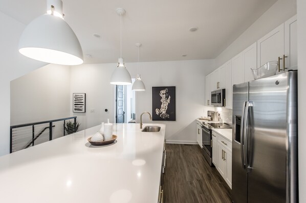A modern kitchen with white cabinets, stainless steel appliances, pendant lighting, and artwork on the walls. - Brand new 4 BR, 4Bath Townhome with amazing rooftop! (Nashville)