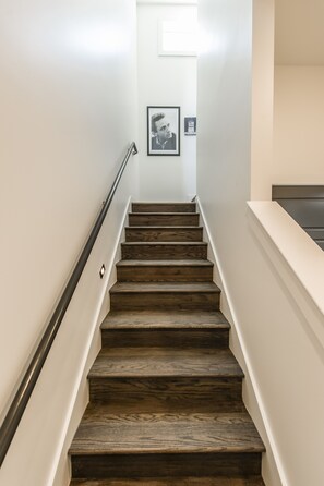A wooden staircase with a handrail, leading to a landing with a framed picture and a small plaque.