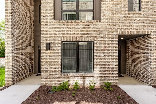A modern building with a brick facade, a central window, and a small garden area with plants. - Brand new 4 BR, 4Bath Townhome with amazing rooftop! (Nashville)