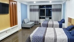 A hotel room with two beds, a sofa, a TV, and a window with curtains. - San Isidro Grand Hotel (Nazca)