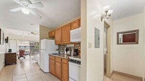 A kitchen with wooden cabinets, a white refrigerator, a stove, and a microwave. There is a ceiling fan, a dining area with chairs, and a view of the outside.