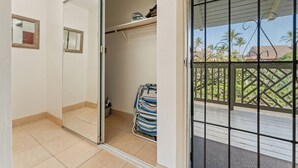 A room with a sliding door leading to a balcony, a tiled floor, and a small storage area with a blue and white striped bag.