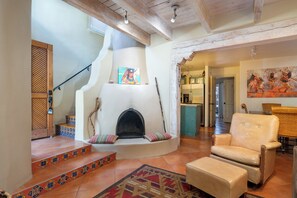 A living room with a fireplace, a sofa, and a chair. There is a staircase with patterned tiles leading to another room. - Las Brisas 31 by Kokopelli Property Management (Santa Fe)
