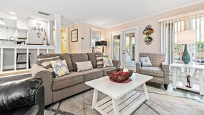 A living room with a sofa, armchair, coffee table, and a dining area with a table and chairs. - Saint Andrews Common 1774 by Hilton Head Retreats (Hilton Head Island)