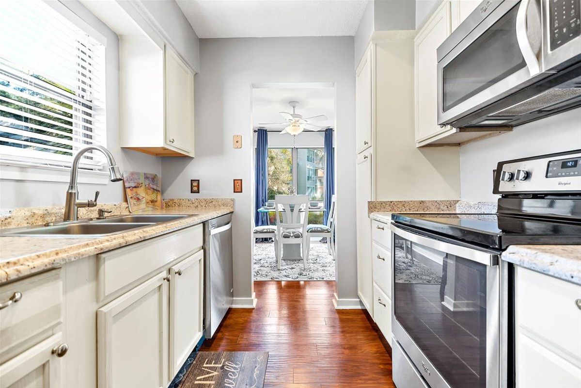 A kitchen with white cabinets, a microwave, an oven, and a sink.