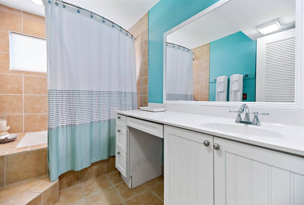 Een badkamer met een witte wastafel, een spiegel, een douchegordijn en een bad.