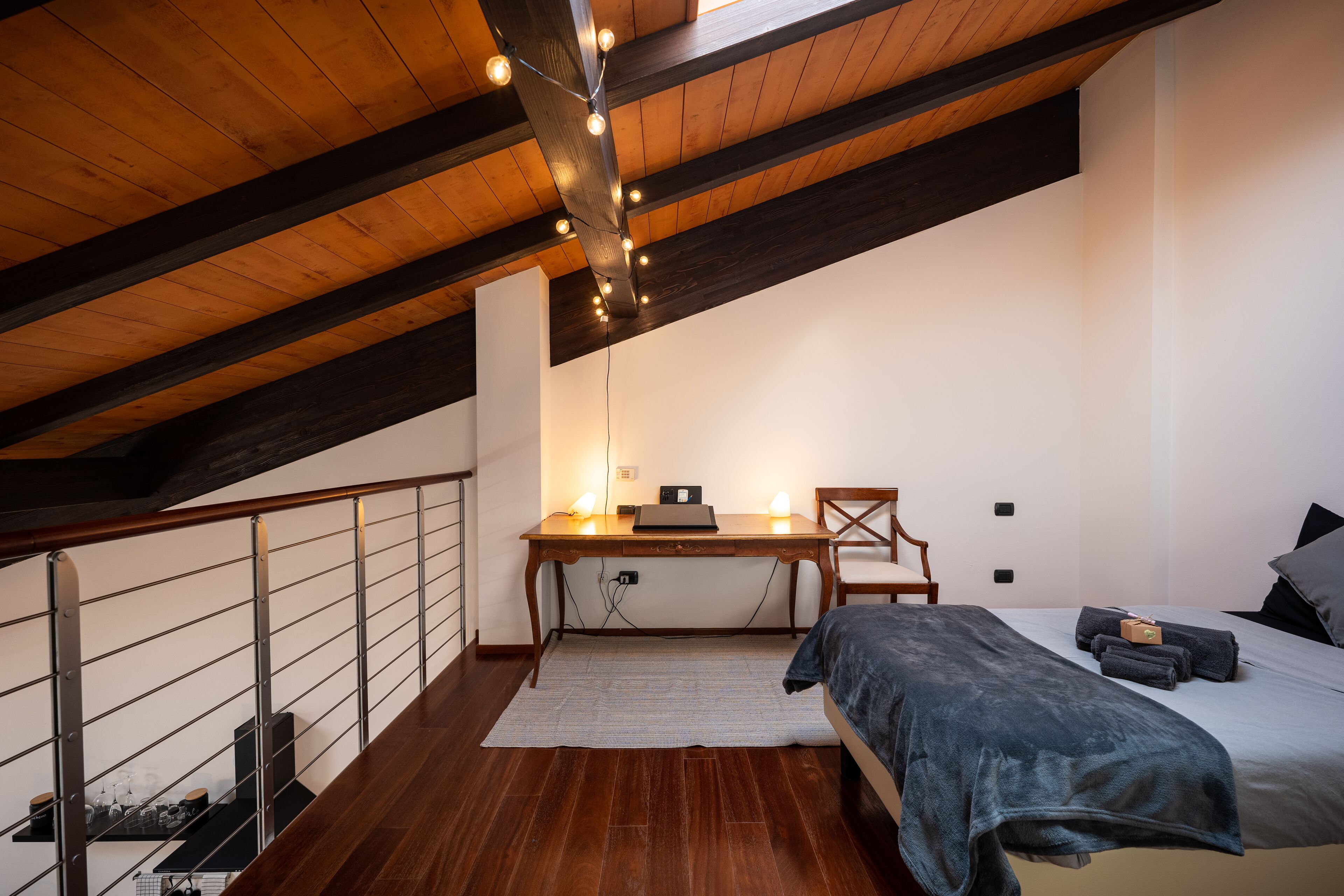 A bedroom with a wooden ceiling, a desk with a laptop, a bed with a blanket, and a chair.