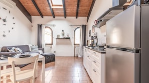 A modern kitchen with a stainless steel refrigerator, a dining area with a table and chairs, and a living area with a sofa.