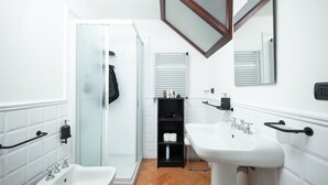 Een badkamer met een bidet, twee wastafels, een spiegel en een douchecabine met glazen wanden.