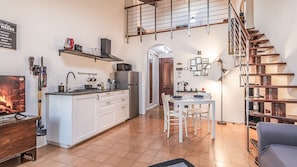 A modern kitchen with white cabinets, a dining area with a white table and chairs, a fireplace, and a staircase leading to an upper level.