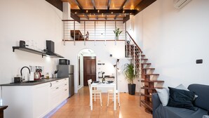 Een moderne keuken met witte kastjes, een eettafel met stoelen, een trap en een zithoek met een bank.