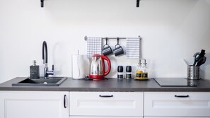 A kitchen counter with a sink, a red kettle, hanging pots, and various kitchen items.