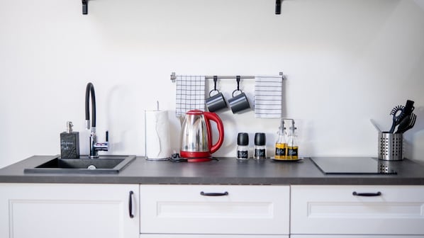 A kitchen counter with a sink, a red kettle, hanging pots, and various kitchen items.