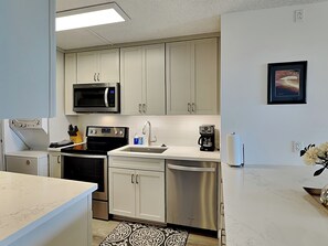 Una cocina moderna con gabinetes blancos, electrodomésticos de acero inoxidable, un microondas, un horno, un lavavajillas y una cafetera.