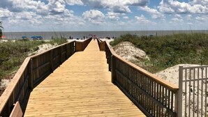 Une promenade en bois menant à une plage, avec un ciel dégagé et quelques nuages.