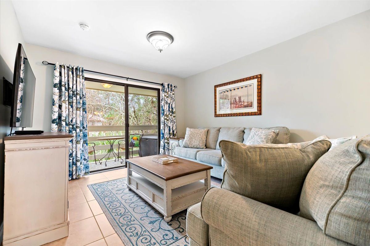 A living room with a sofa, a coffee table, a TV, and a sliding glass door leading to a balcony.