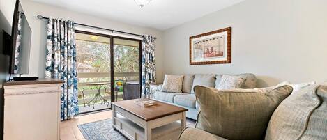 A living room with a sofa, a coffee table, a TV, and a sliding glass door leading to a balcony.