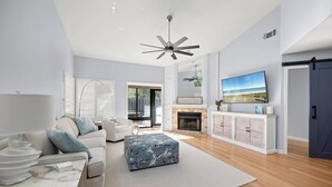 A modern living room with a sofa, ottoman, fireplace, television, and a ceiling fan. - Loggerhead Lodge by Distinctive Beach Rentals (Ponte Vedra Beach)