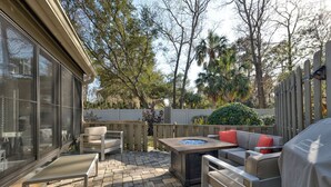An outdoor patio with a fire pit, seating, and a view of the surrounding trees. - Loggerhead Lodge by Distinctive Beach Rentals (Ponte Vedra Beach)