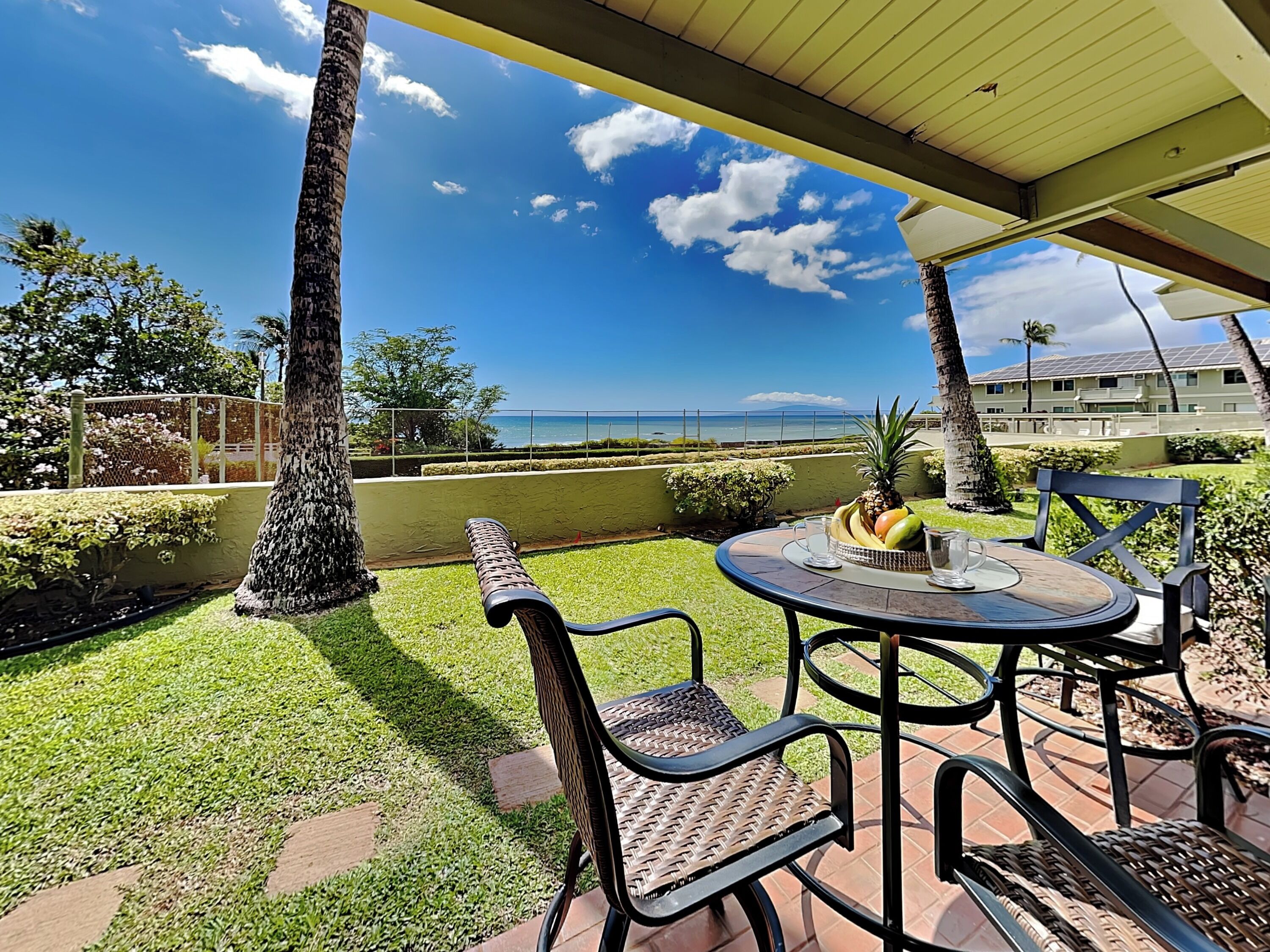 A patio with a table and chairs, a fruit bowl, and a view of the ocean.