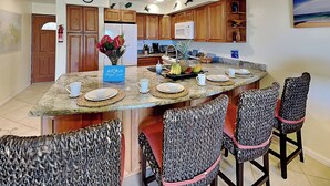Una cocina moderna con armarios de madera, una isla central con taburetes de bar y un reloj en la pared.