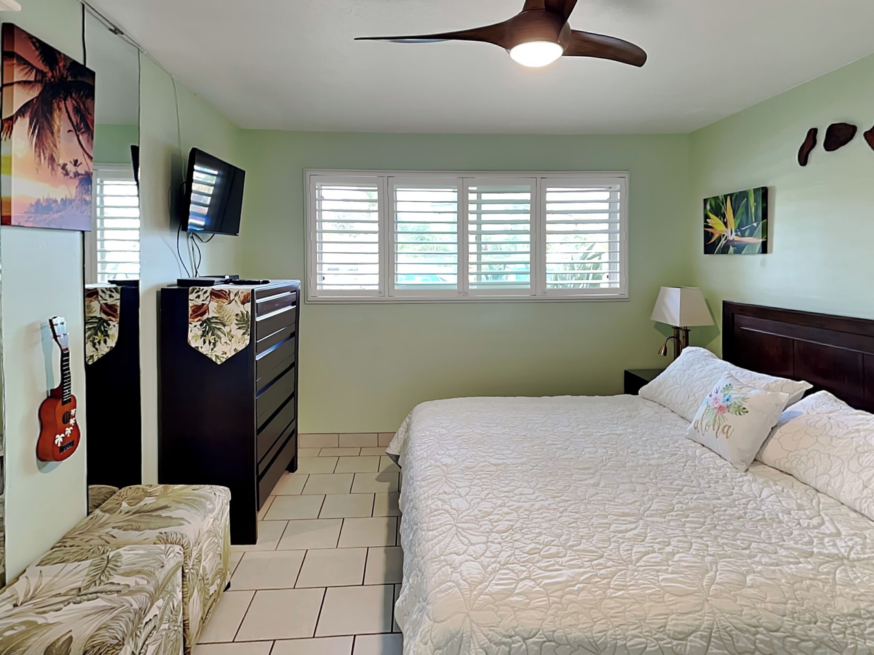 A bedroom with a bed, a dresser, a television, a guitar, and a window with blinds.