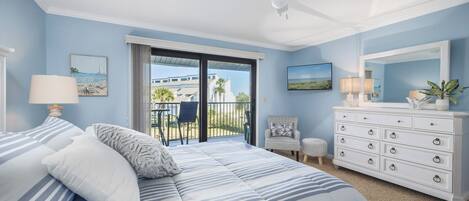 A bedroom with a bed, a dresser, a chair, a small table, and a balcony with a view.