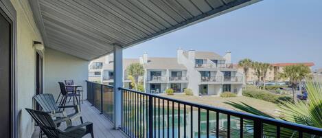 A balcony with outdoor furniture, a pool, and a view of multi-story buildings.