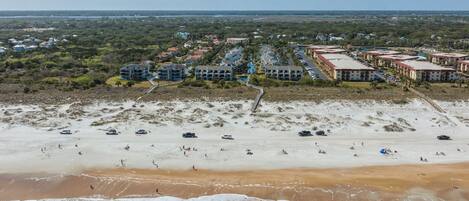 A coastal area with a sandy beach, a row of beachfront buildings, and a distant view of a city skyline.