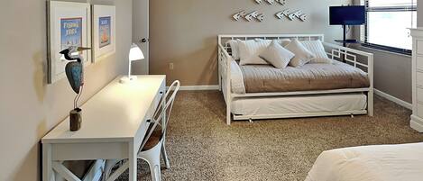 A bedroom with a bed, a desk, and a chair. There are wall decorations and a window with blinds.