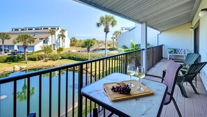 A balcony with a table set for a meal, overlooking a body of water and a building with palm trees. - Sea Winds 51 by Distinctive Beach Rentals (St. Augustine)