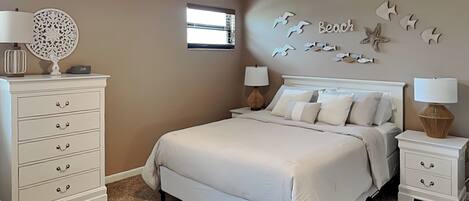 A bedroom with a large bed, two bedside tables with lamps, a dresser, a ceiling fan, and a wall decoration with seagulls and fish.