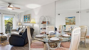Een eetruimte met een glazen tafel, witte stoelen en een plafondventilator.