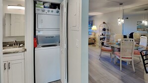 Een compacte keuken met een ingebouwde wasmachine en droger, een eethoek met tafel en stoelen, en een klein zitgedeelte met een lamp.