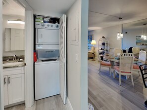A compact kitchen with a built-in washer and dryer, a dining area with a table and chairs, and a small seating area with a lamp.