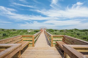 Walk along the boardwalk to the beach, flanked by benches and a metal gate.